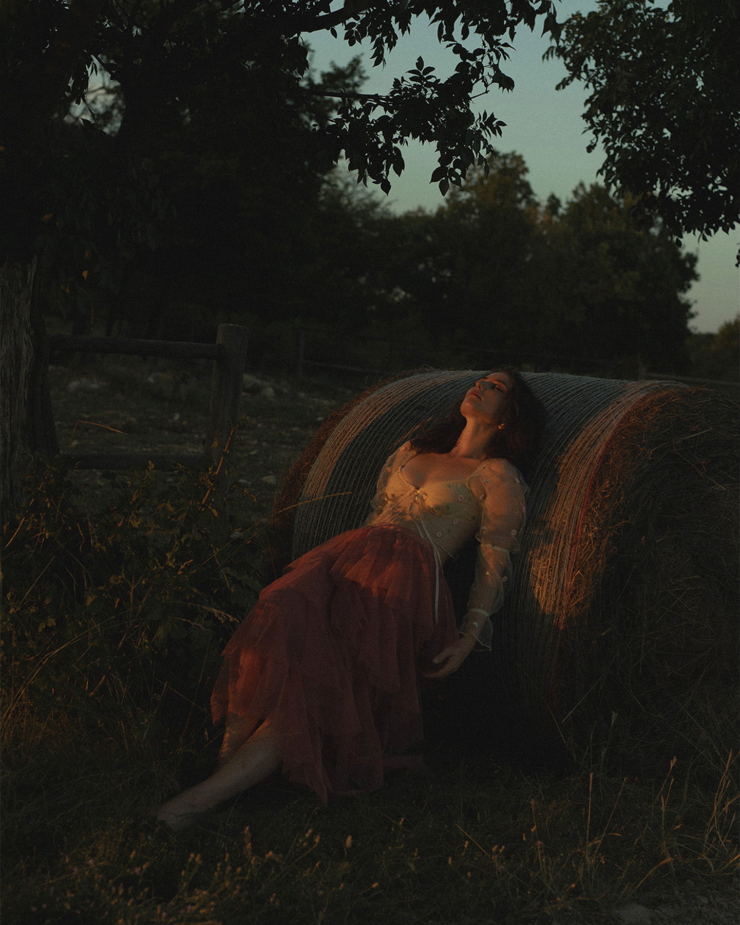 Editorial portrait at dusk beside a hay bale