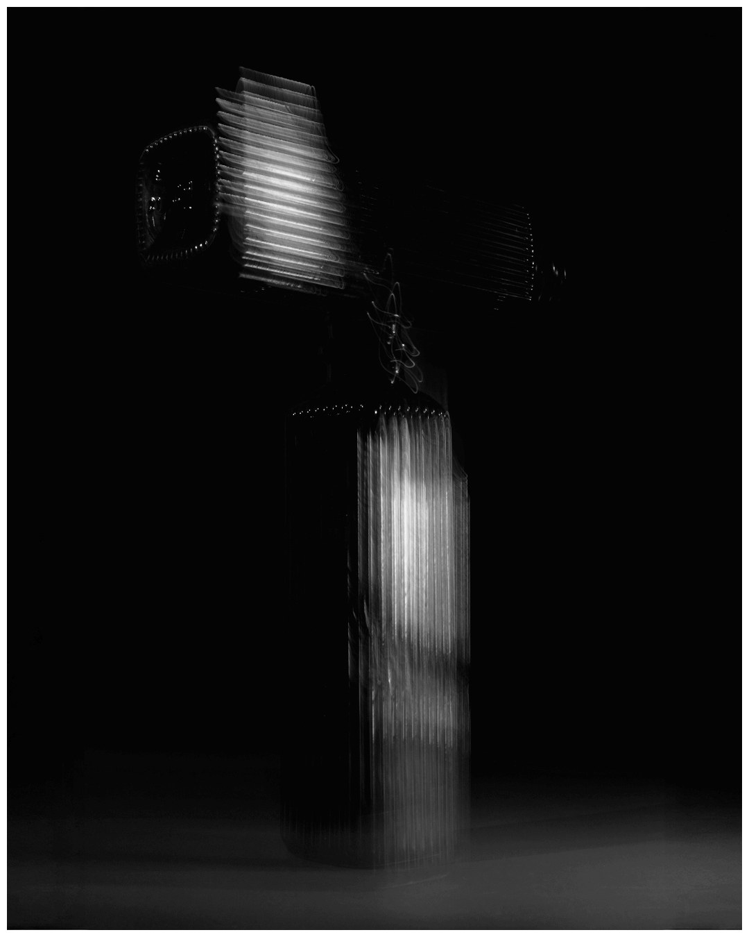 Black and white motion study of a ribbed glass vessel on a dark background