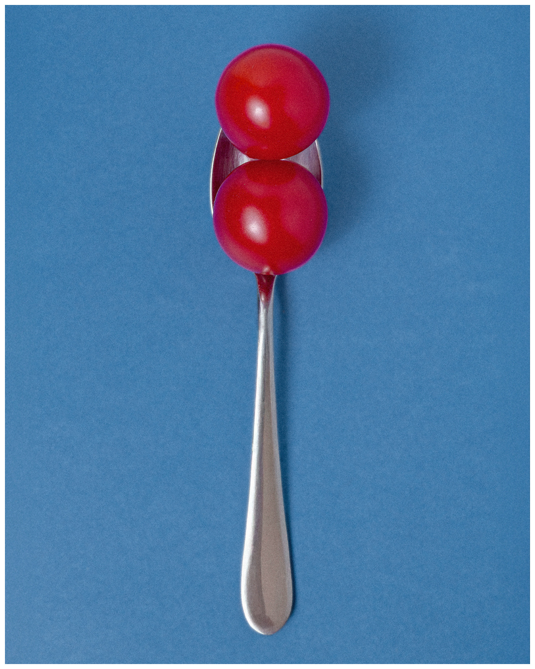Two red tomatoes balanced on a spoon against blue