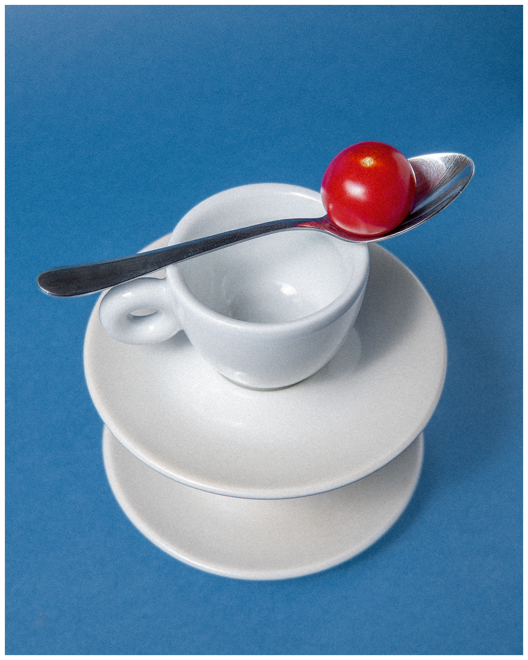 White cups and plates stacked with a tomato balanced on a spoon